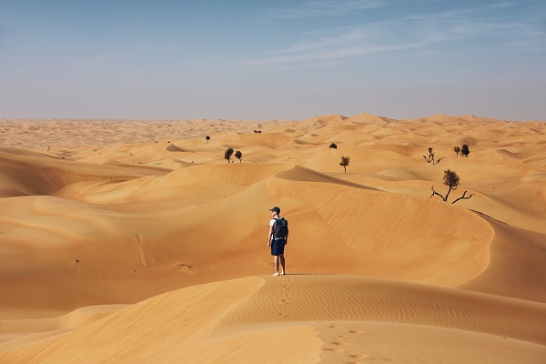 Young man standing on sand dune in the middle of desert. Abu Dhabi, United Arab Emirates